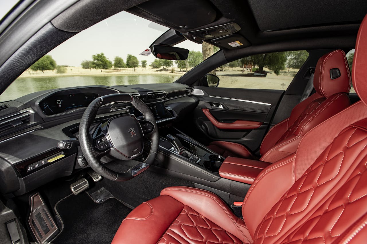 Luxurious car interior featuring red leather seats and sleek dashboard design overlooking a serene outdoor view.