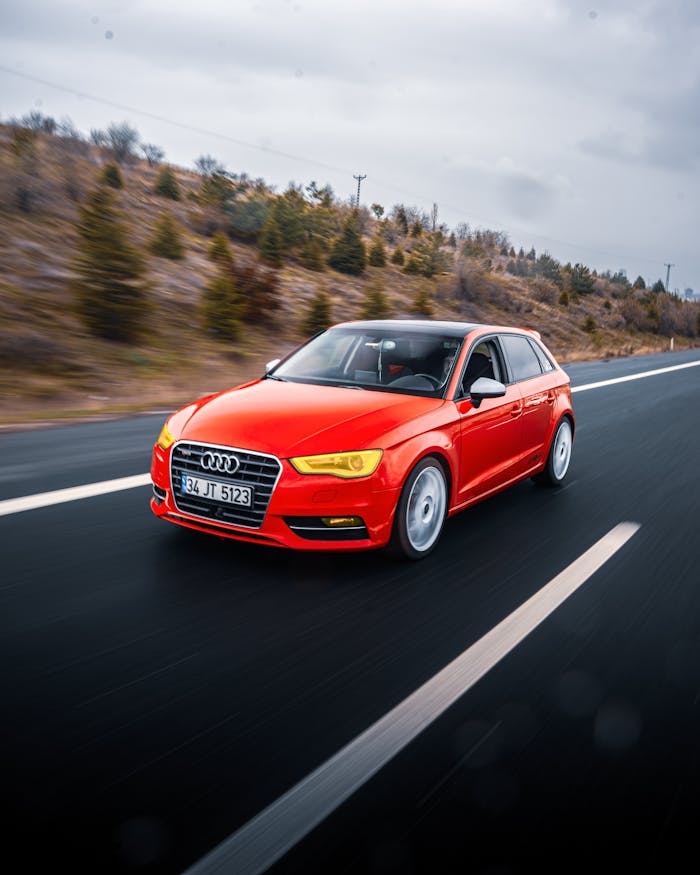 Red Audi A3 driving on a scenic road in Ankara, Türkiye under cloudy skies.